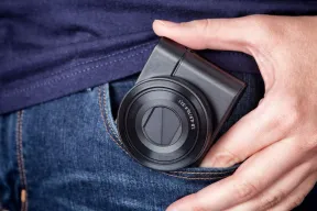 A hand pulling a compact camera from a jeans pocket, where an iPhone would usually sit