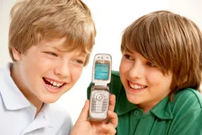 Two smiling kids sharing an open silver flip phone