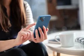 A woman holding a blue iPhone, with a white cup on the table beside her
