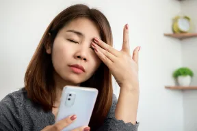 A woman rubbing her eye while holding a phone in a bright room