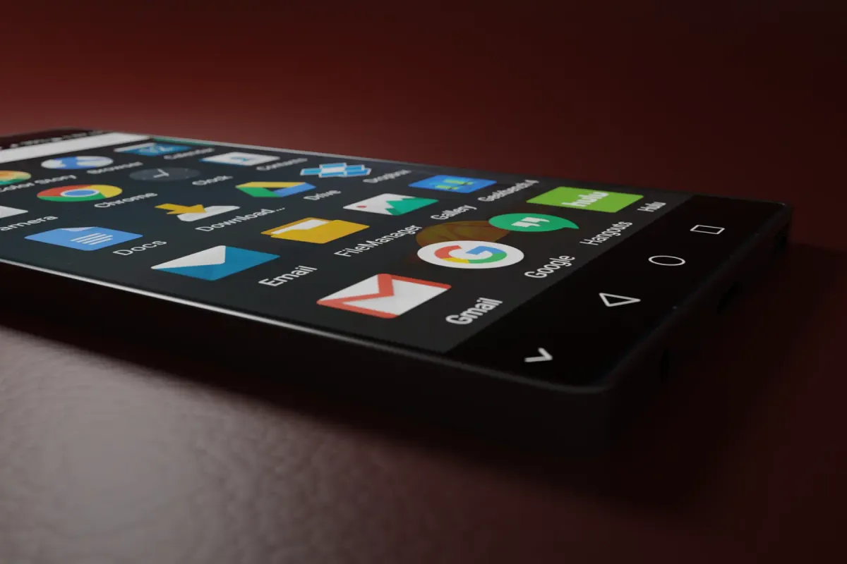 An Android phone lying on a dark red surface with its app drawer of Google apps open