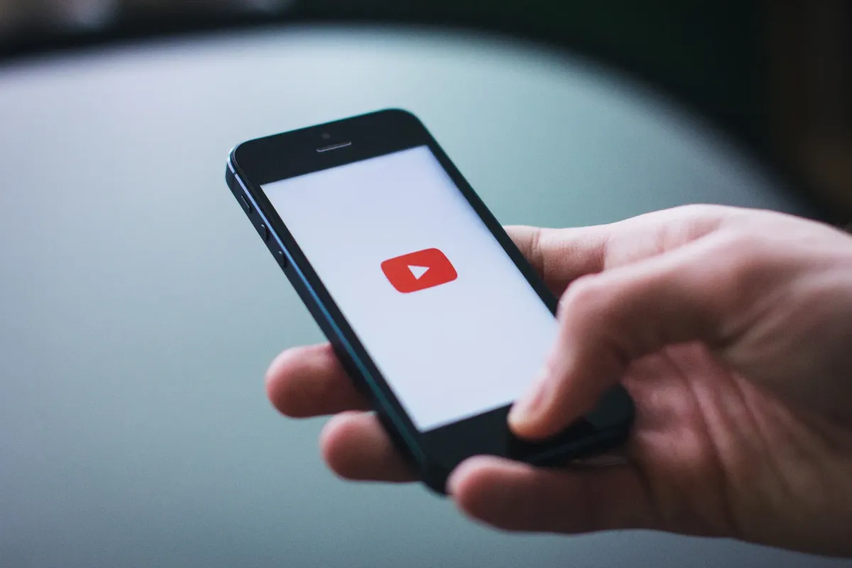 A hand holding an iPhone with the YouTube logo on its screen