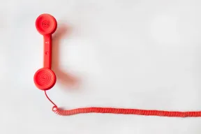A red landline handset with its coiled cord stretched across a white surface