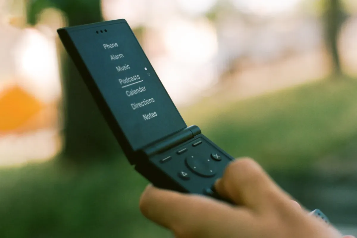 A hand holding the open Light Flip, its screen showing a short menu of tools such as Phone, Alarm, and Directions