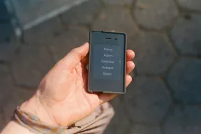 A hand holding the small Light Phone II, whose text-only screen shows a short menu of tools